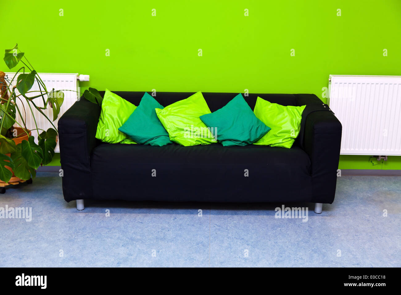 Un sofá negro en un salón ante una pared verde, Eine schwarzes Sofá en einem Wohnzimmer vor einer gruenen Wand Foto de stock