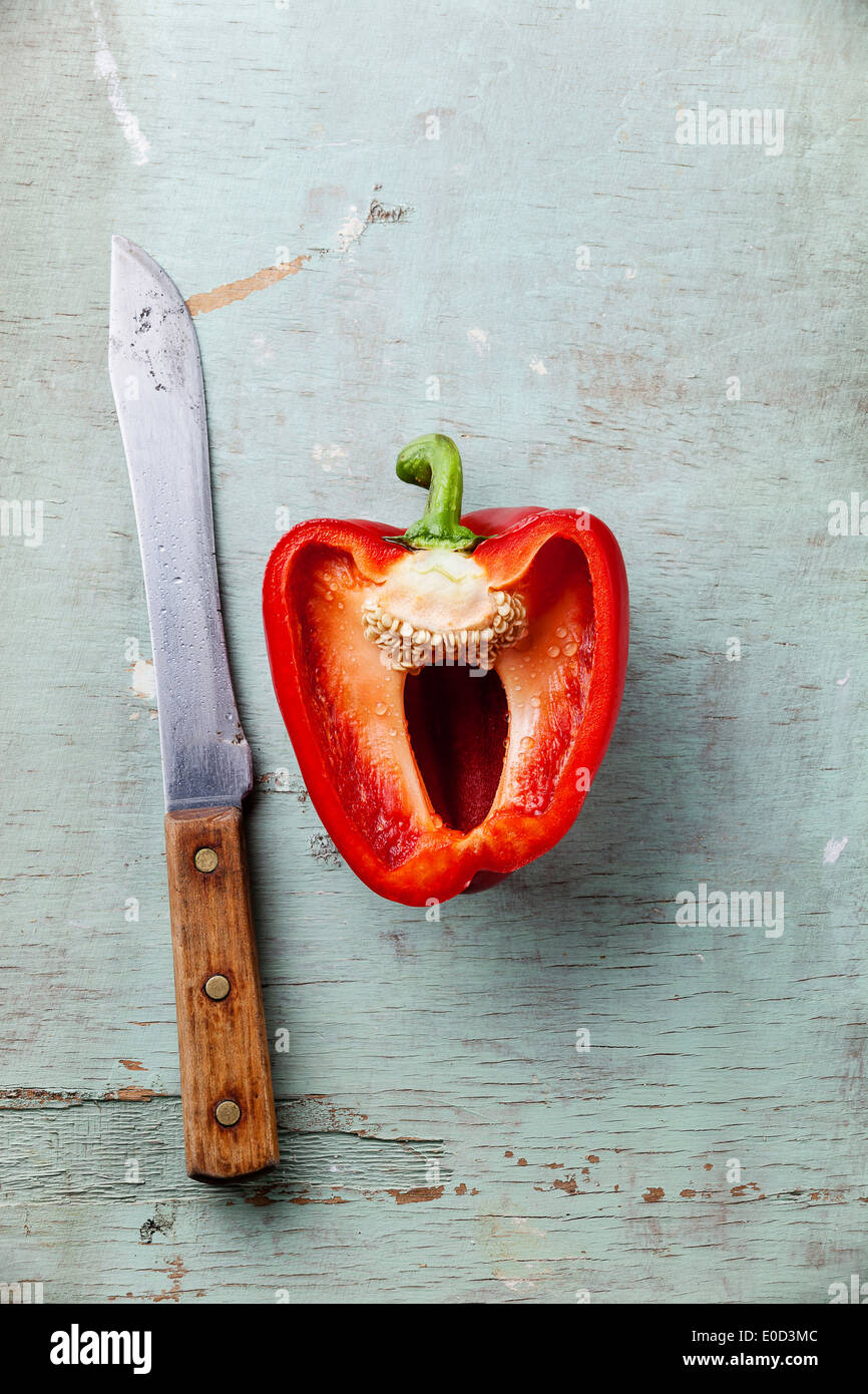 La mitad del pimiento rojo y el cuchillo en la textura de fondo azul Foto de stock