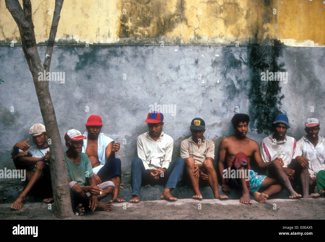 Desempleados hombres sentados por un muro en Yakarta, Indonesia Foto de stock