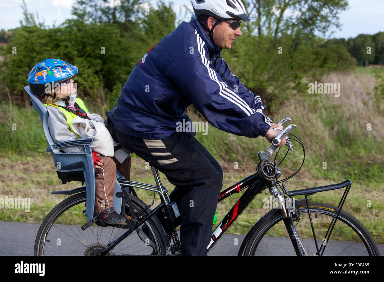 Paseo de hombre y niño, casco de bicicleta, sendero para bicicletas, niño en el asiento de bicicleta Foto de stock