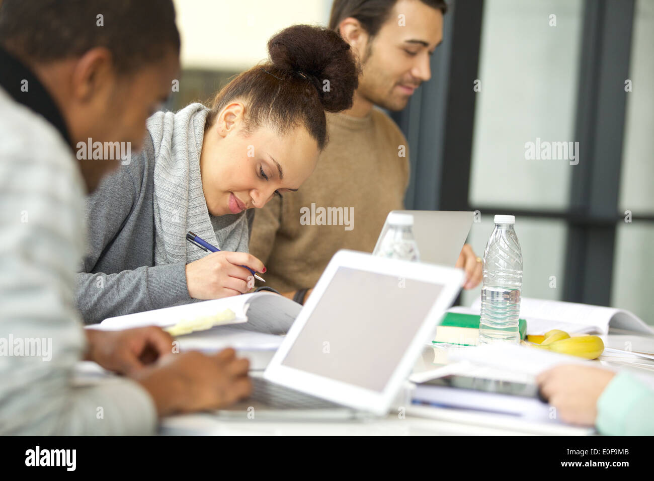 Joven afroamericana tomando notas de libros para su estudio. Estudiantes sentados a la mesa con libros y laptop estudiando. Foto de stock