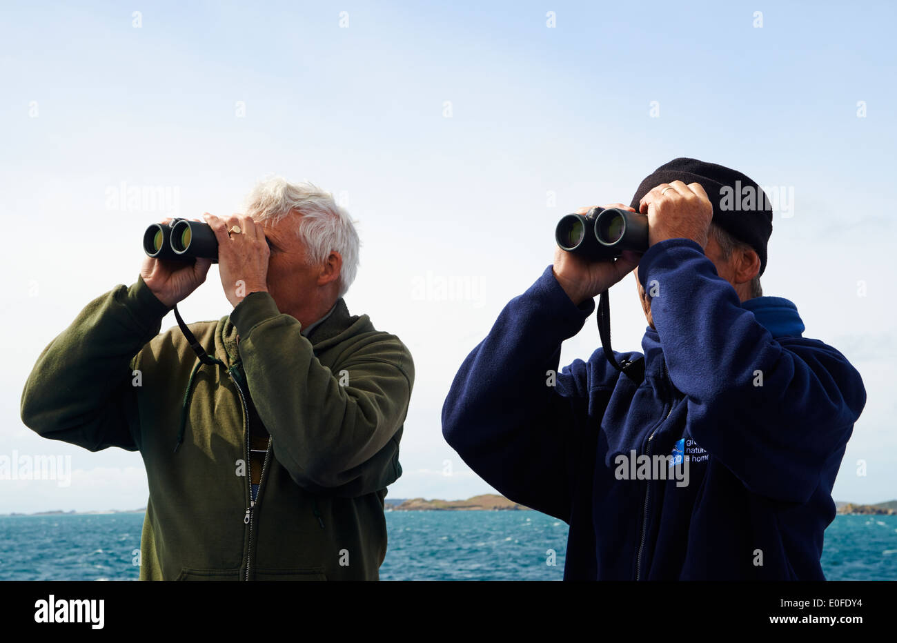 Dos hombres la gente de RSPB con prismáticos observando las aves en el ferry boat trip Scillonian III de Islas Scilly, Scillies, Cornwall en abril Foto de stock