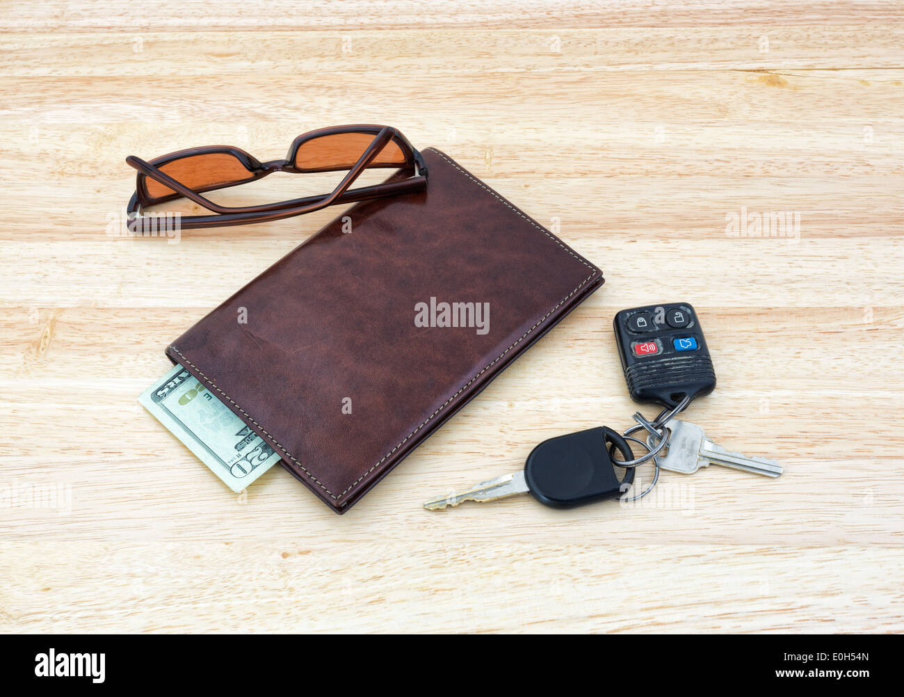 Un conjunto de llaves del coche con gafas de sol sobre una mesa de madera con un monedero de cuero y efectivo. Foto de stock