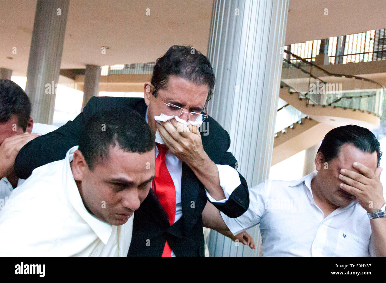 Tegucigalpa, Honduras. El 13 de mayo de 2014. El ex presidente de Honduras, Manuel Zelaya (C) cubre su rostro de gas lacrimógeno tras ser evacuado con sus seguidores del Congreso Nacional, en Tegucigalpa, Honduras, el 13 de mayo de 2014. Seguidores y diputados del Partido libertad y Refundación (Libre, por sus siglas en inglés), la segunda fuerza política en Honduras, irrumpieron en el Congreso Nacional el martes, después de chocar con los elementos de policía que protegía el Palacio Legislativo. Crédito: Rafael Ochoa/Xinhua/Alamy Live News Foto de stock
