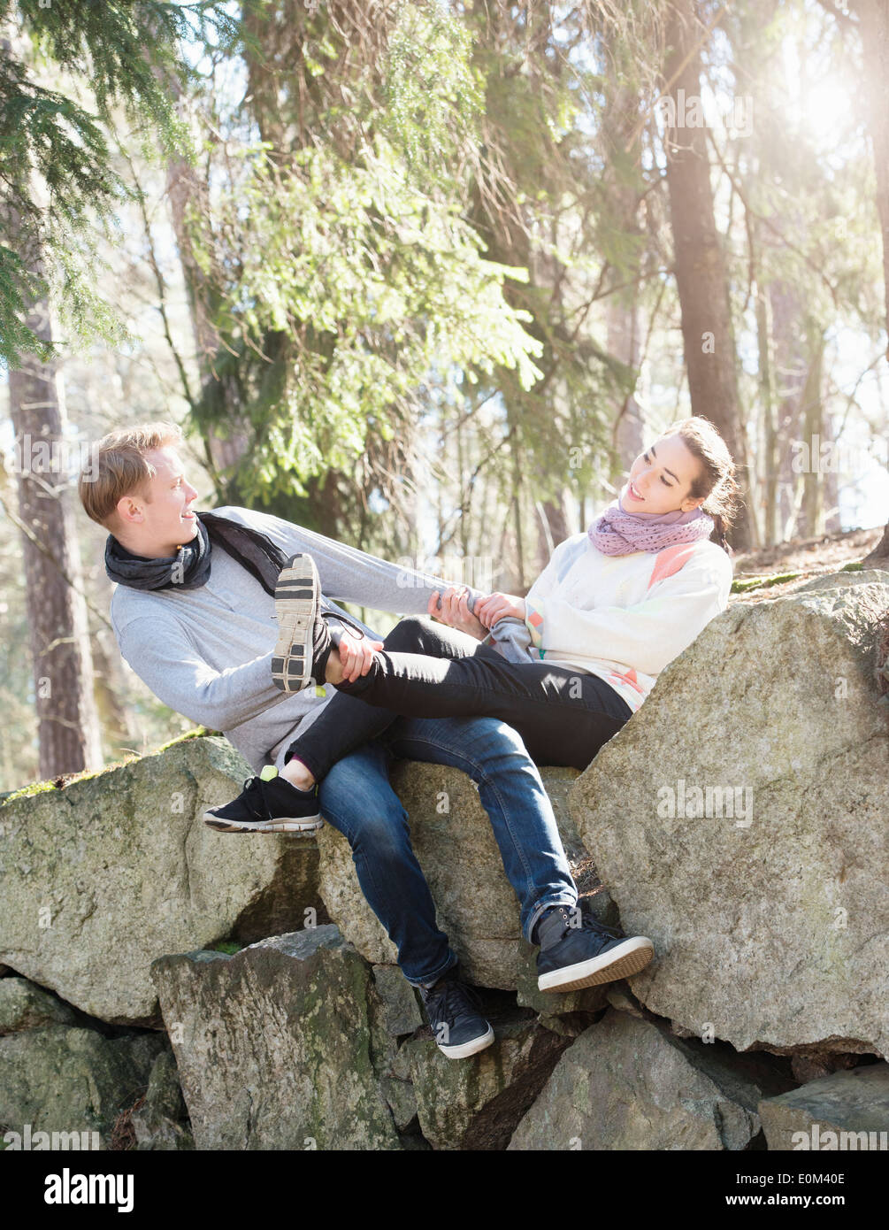 Pareja joven en la naturaleza descansa sobre grandes rocas en los bosques durante una caminata. Divertido juego en el borde de una gran roca. Foto de stock