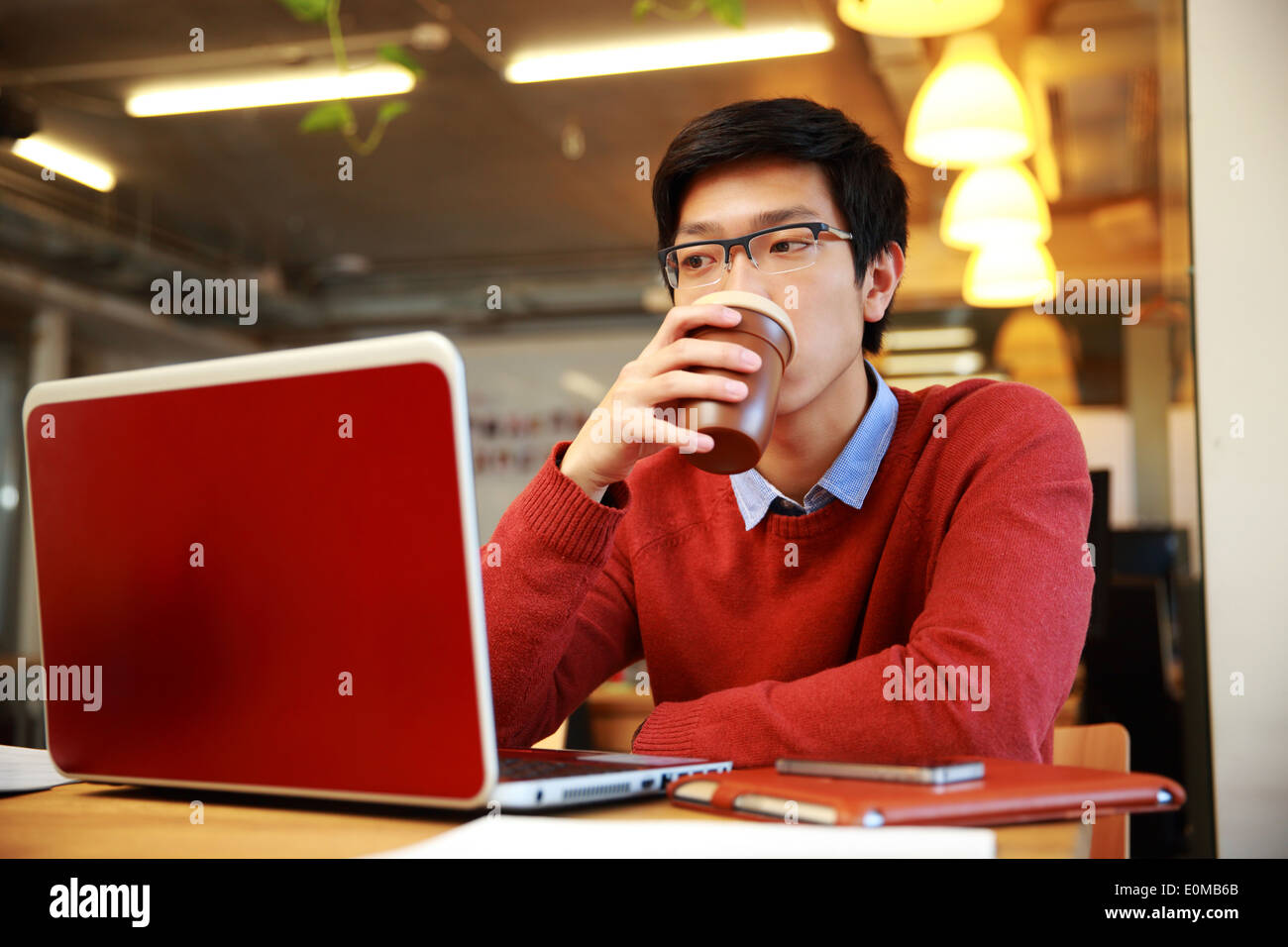 Apuesto hombre asiático trabajando en el portátil y bebiendo café Foto de stock