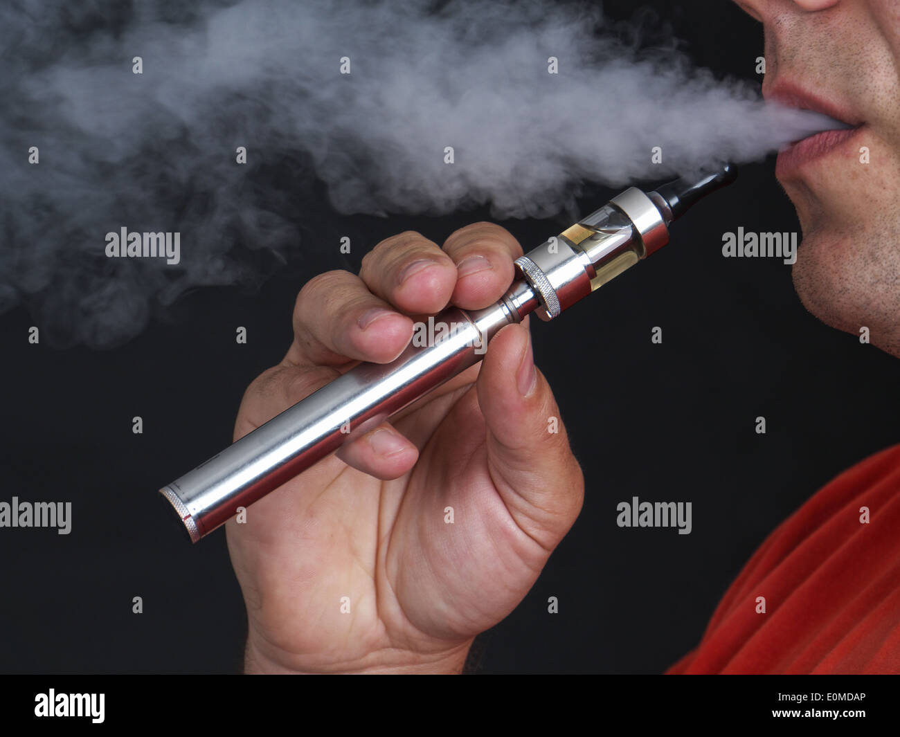 Primer plano del hombre mediante el e-cigarrillo y exhalar vapor shot sobre fondo negro Foto de stock