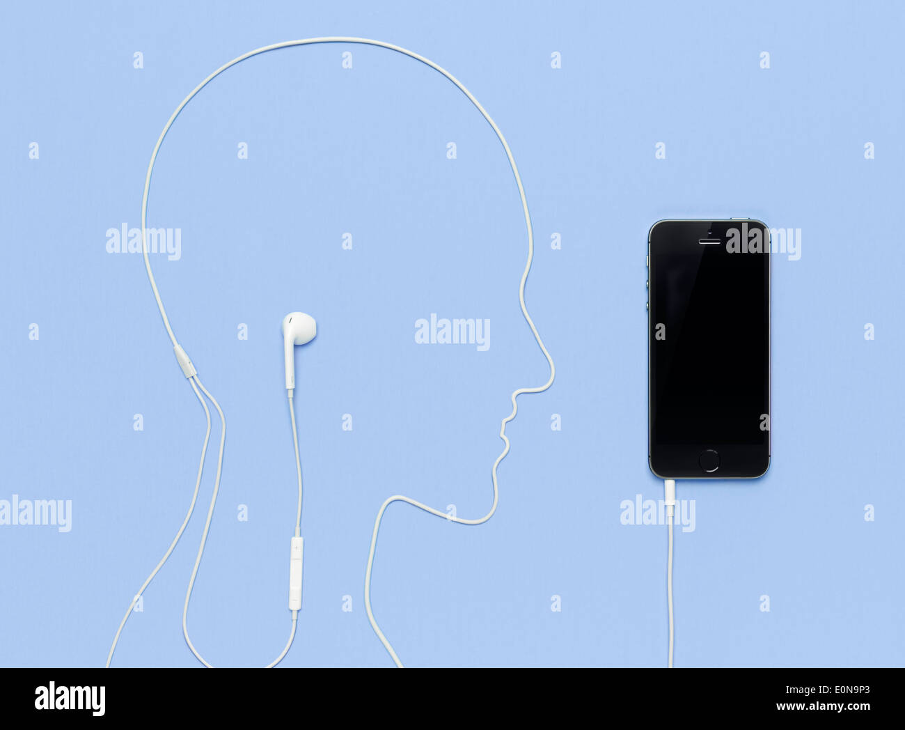 Cabeza de hombre hecha por un esquema del cable de los auriculares enchufados en iPhone 5s smartphone. Concepto de música creativa sobre fondo azul. Foto de stock