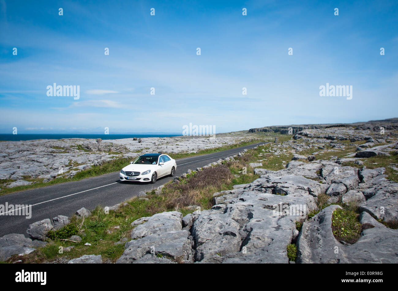 Coche blanco en día soleado en la carretera y recorrer la ruta a través del Burren en el condado de Clare junto a la salvaje forma del Atlántico, en la costa occidental de Irlanda Foto de stock