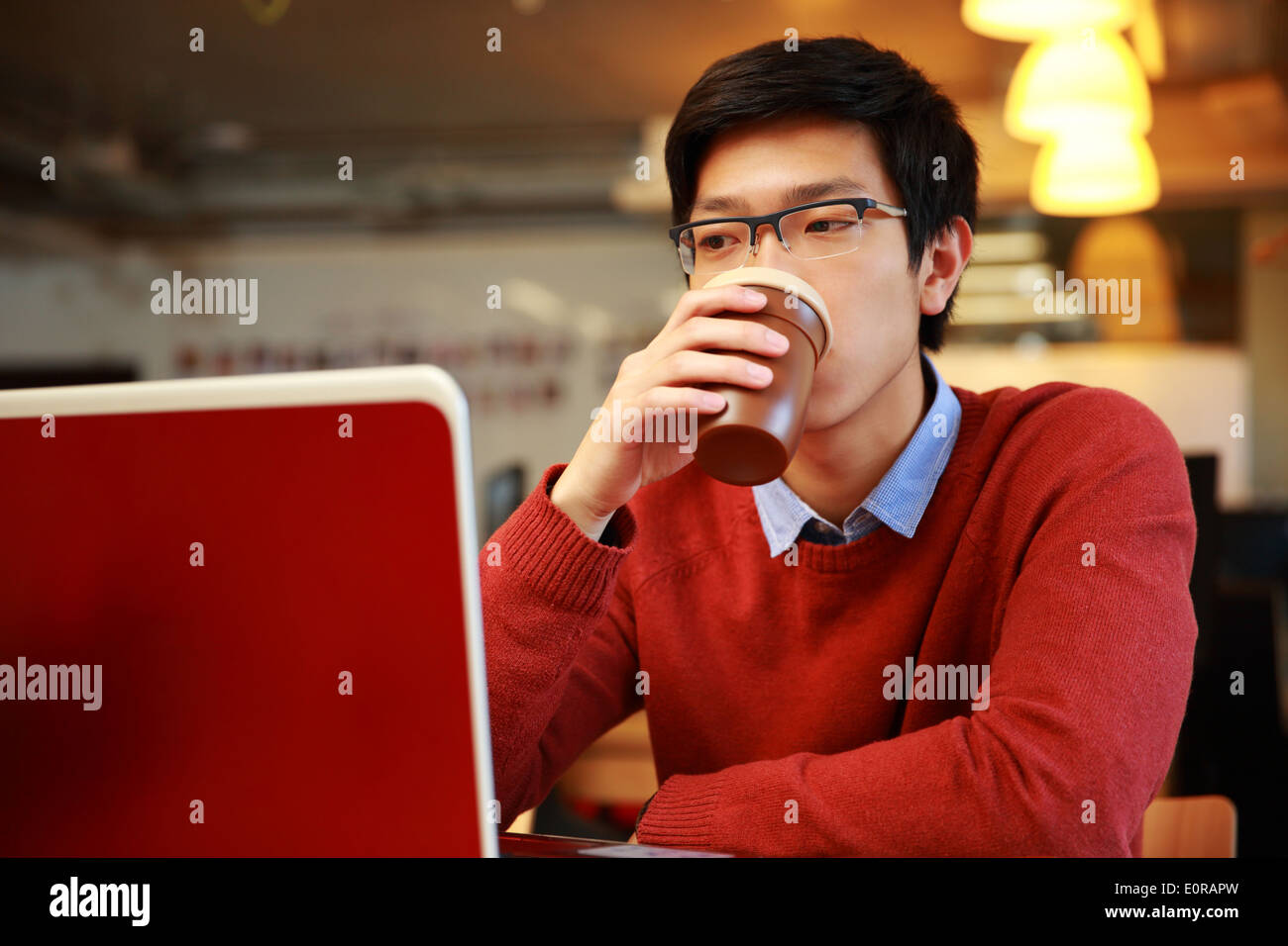 Joven asiático hombre trabajando con un portátil y bebiendo café Foto de stock