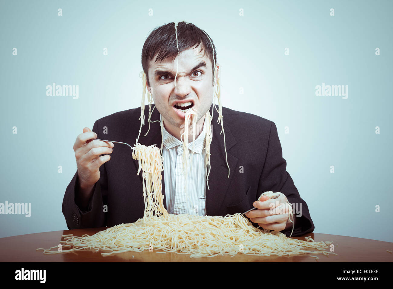 Concepto de consumismo codiciosos. Empresario desagradable comer pasta sobre la mesa. Foto de stock