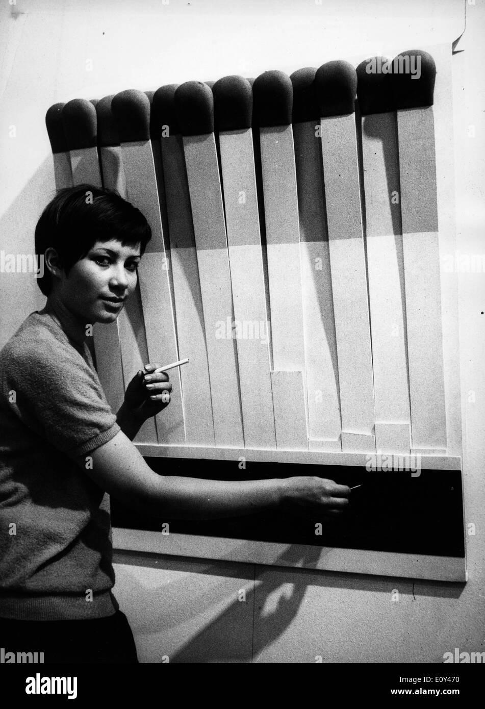 15 Jul, 1968; Munich, Alemania; una mujer pretende encender un cigarrillo newx a una gran caja de cerillas en una muestra de arte en Alemania. Foto de stock