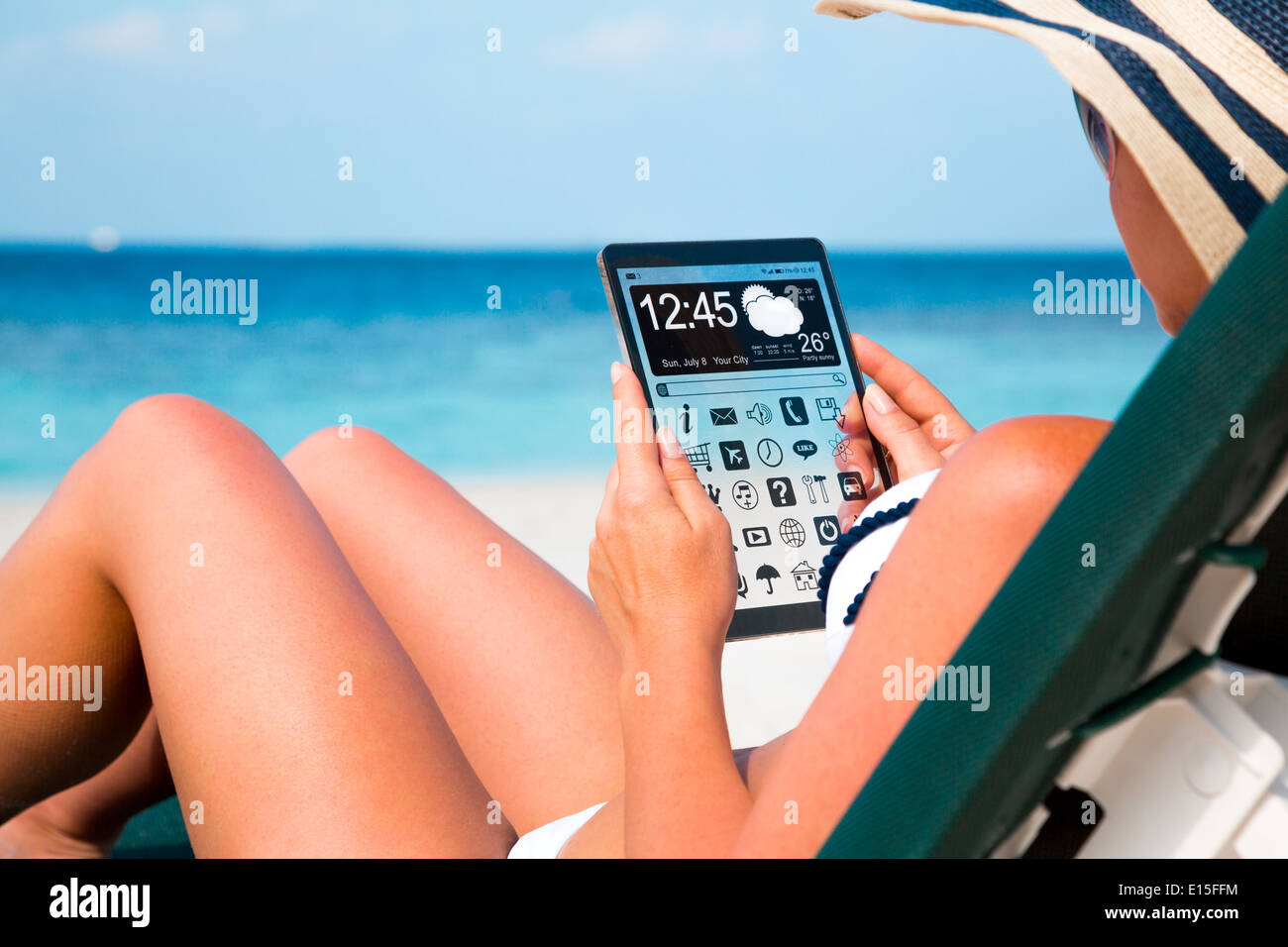 Mujer de vacaciones se encuentra en una tumbona en la playa con una tableta en las manos. Foto de stock