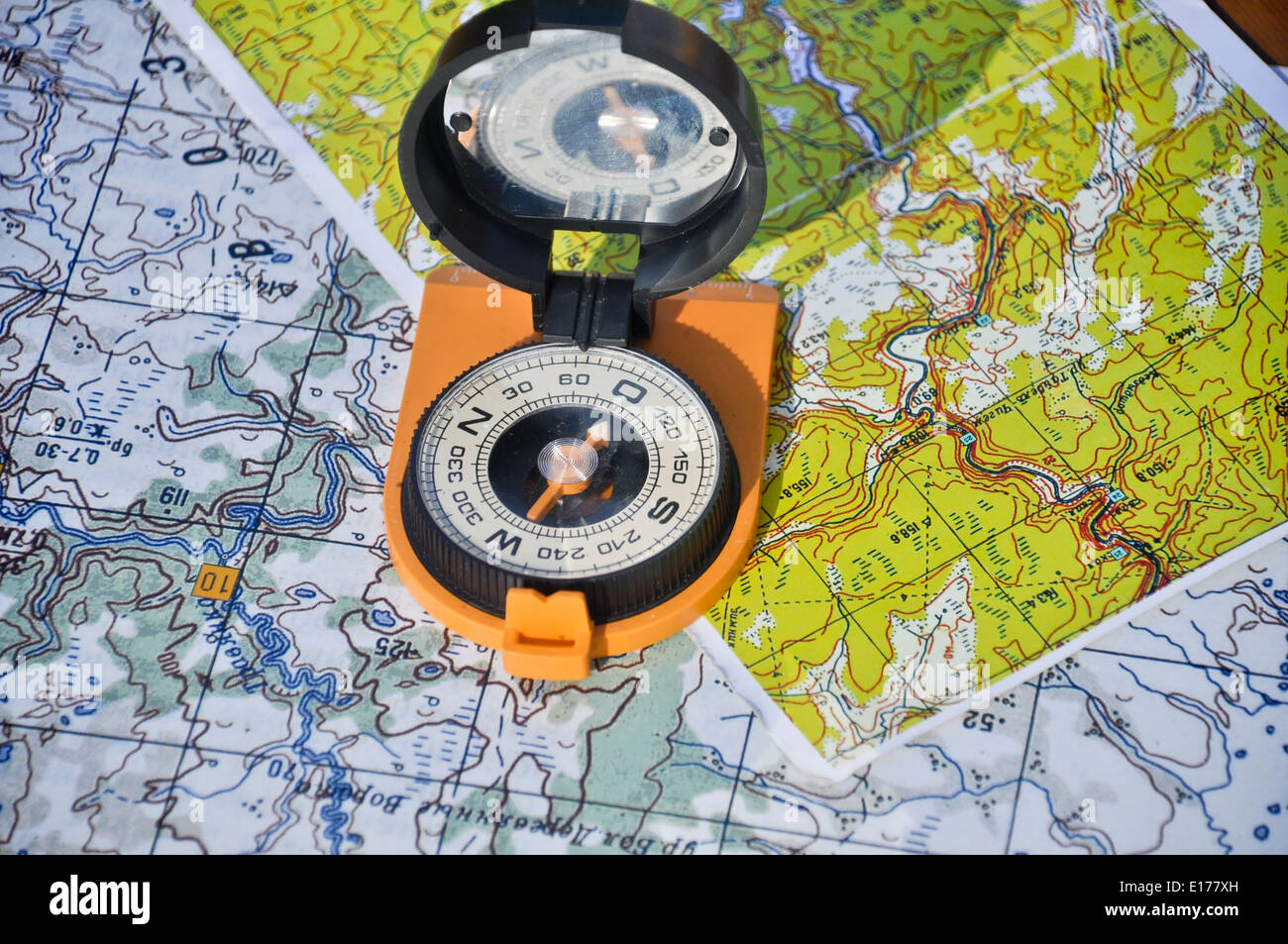 Brújula naranja cubierta del espejo se encuentra en los mapas topográficos. Brújula en el mapa Foto de stock