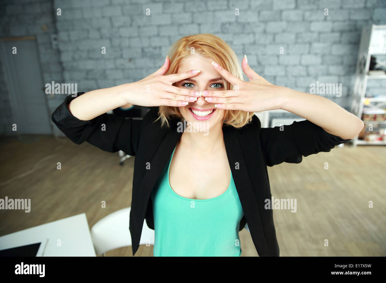Joven mujer alegre mirando a través de los dedos a la cámara en la oficina Foto de stock