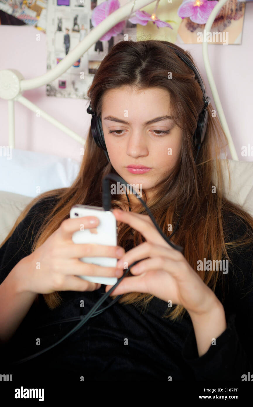 Adolescente escuchando música con los auriculares de su iphone en su cama en el dormitorio. Foto de stock