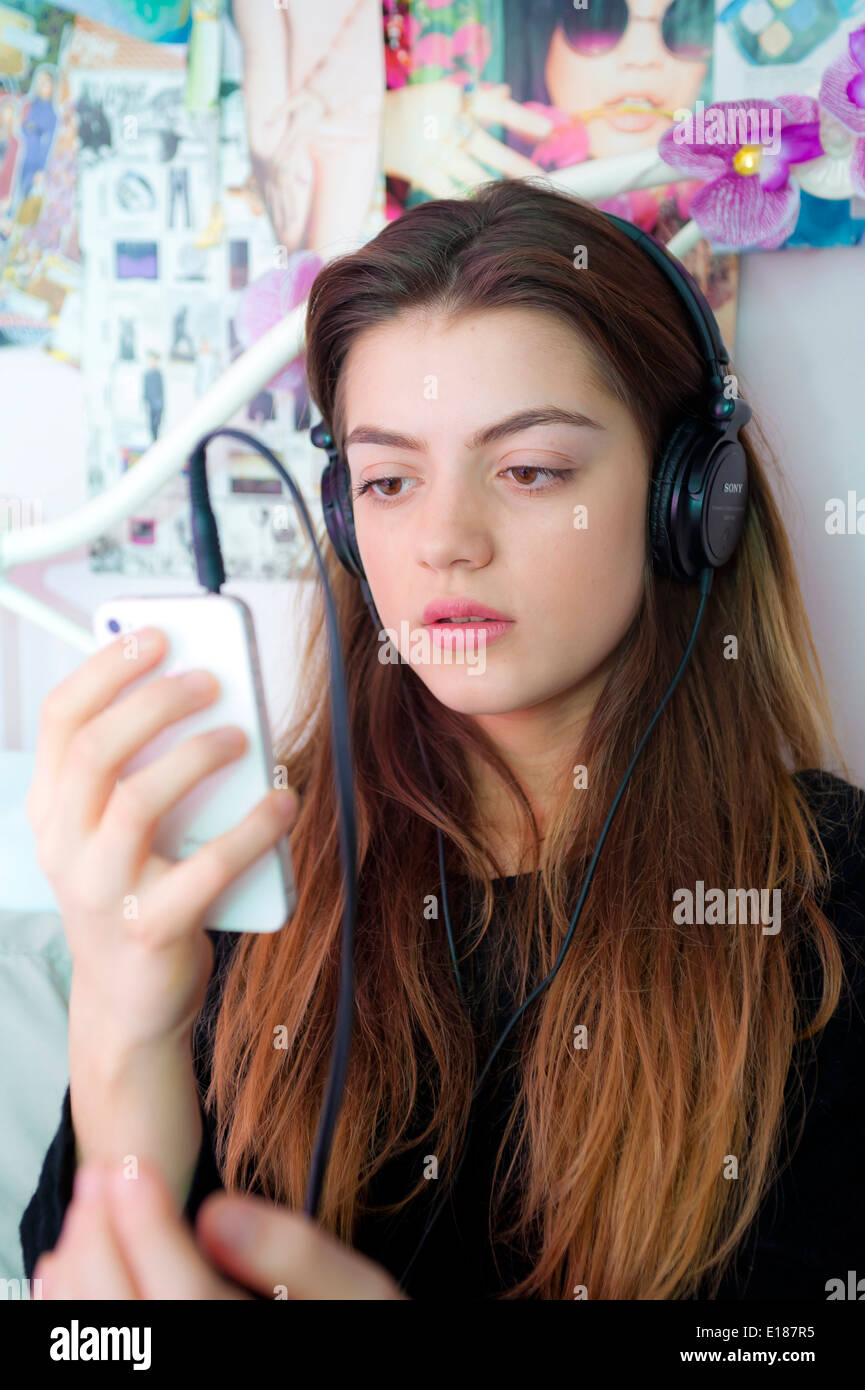 Adolescente escuchando música con los auriculares de su iphone en su cama en el dormitorio. Foto de stock