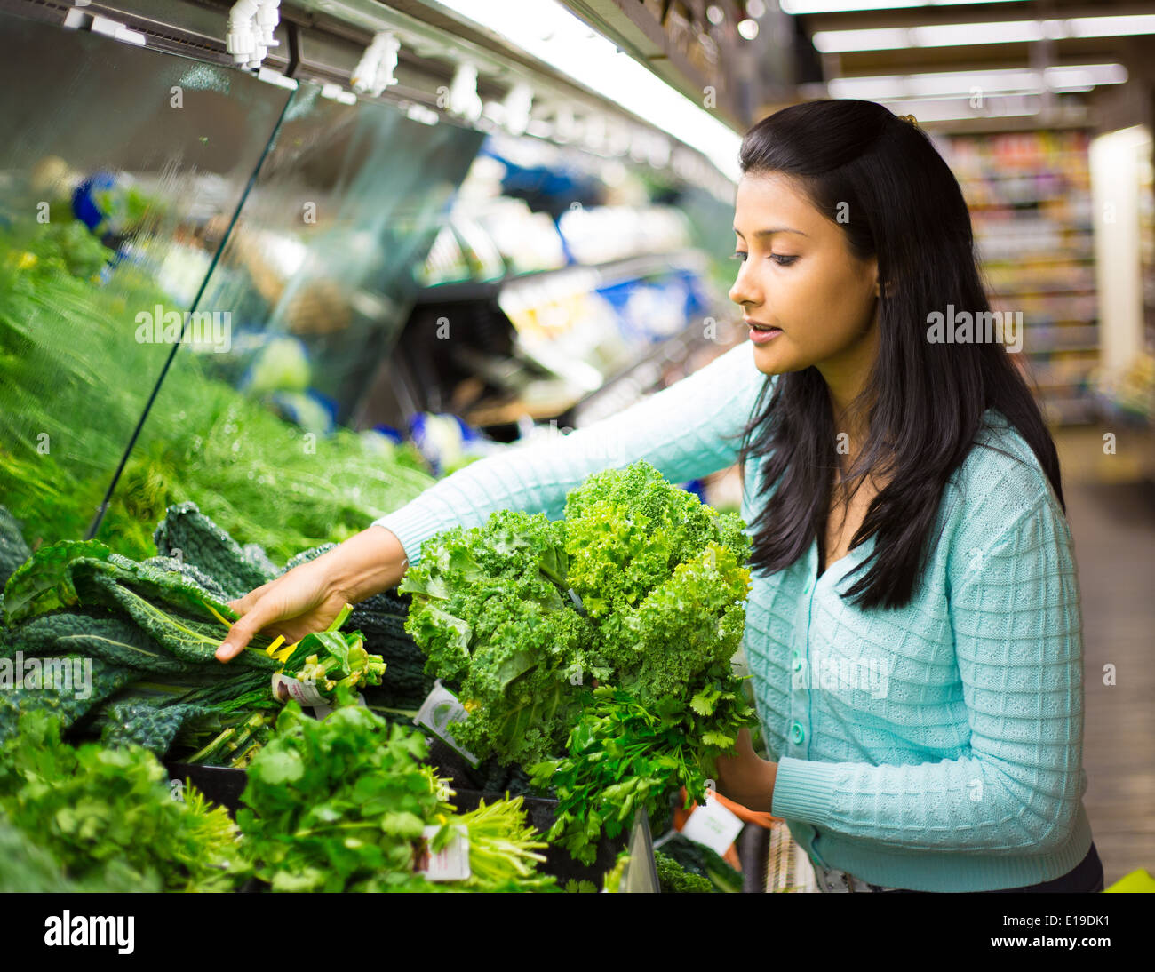 Closeup retrato, hermoso, bastante joven en el suéter de recoger, la elección de las hortalizas de hoja verde en tienda Foto de stock