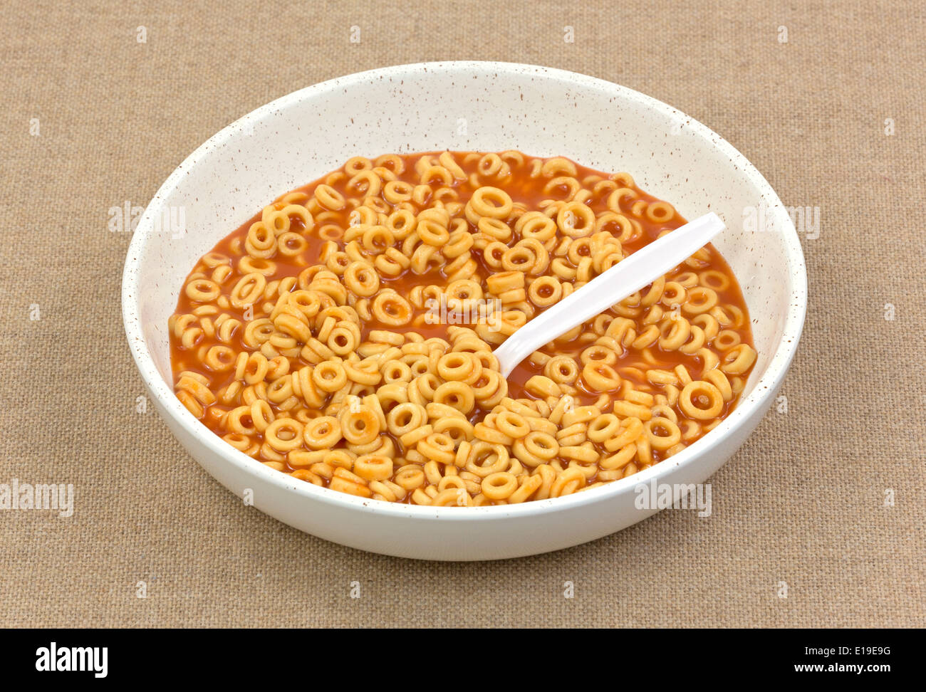 Una porción de conservas de ronda en el cuenco de espaguetis con salsa de tomate y una cuchara de plástico blanca sobre un fondo de tela marrón. Foto de stock
