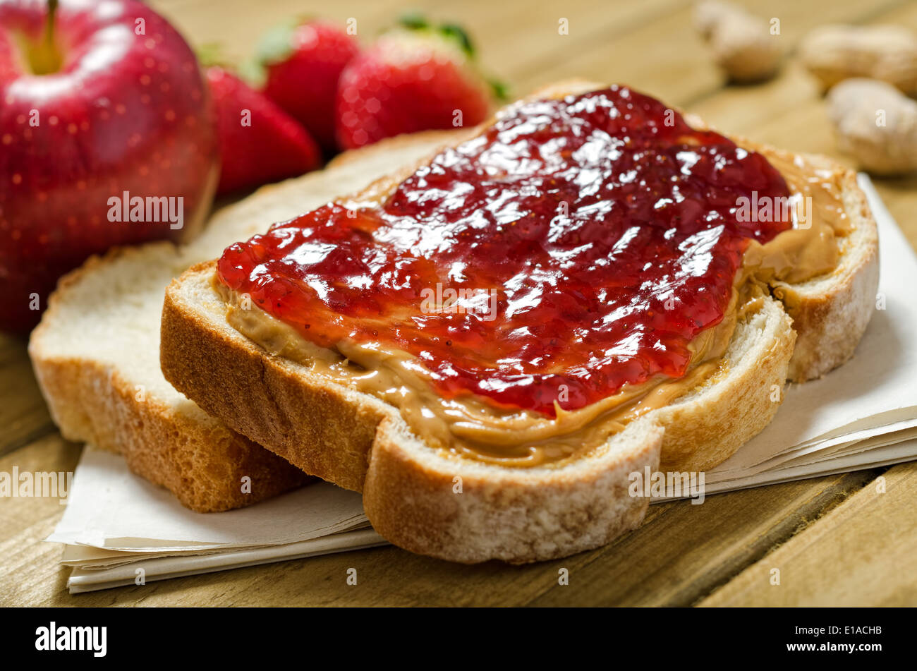 Un nutritivo sándwich de mantequilla de maní y mermelada con las manzanas, las fresas y los cacahuetes. Foto de stock