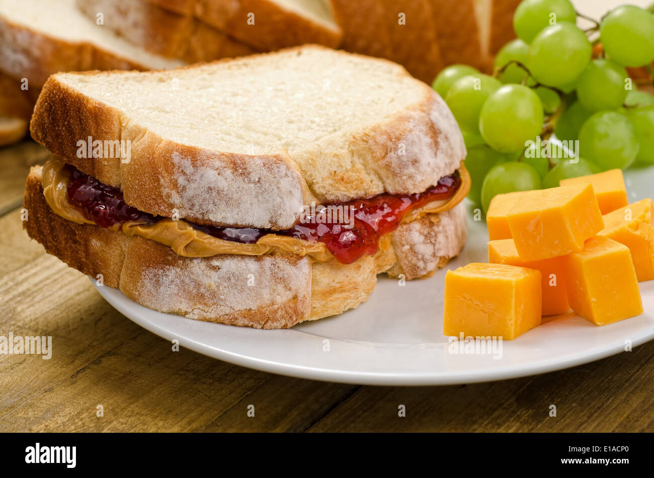 Un nutritivo sándwich de mantequilla de maní y mermelada con queso cheddar y uvas. Foto de stock