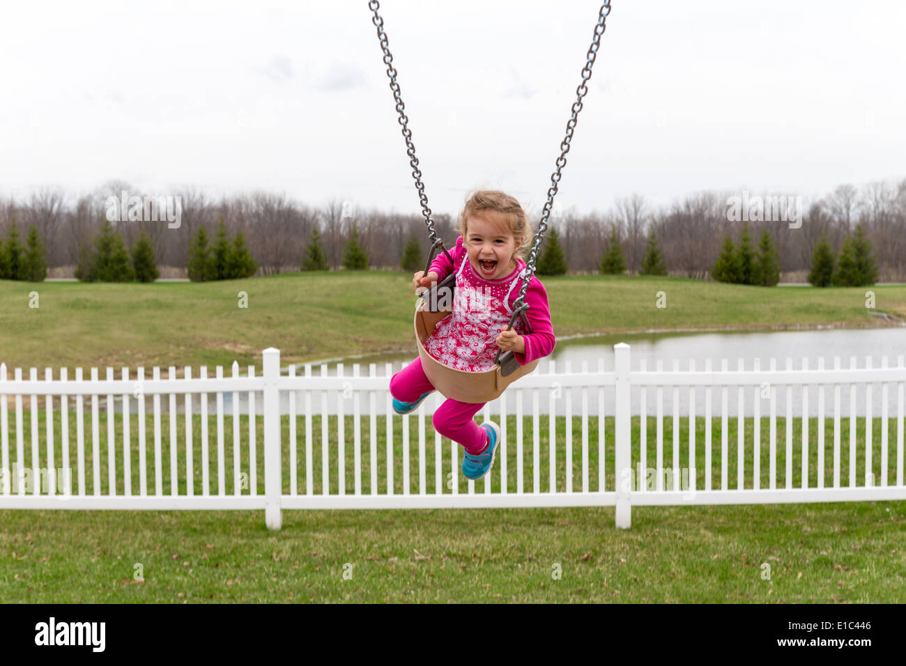 Hermosa niña entusiasmada de balancín de jardín gritando de placer, ríe como ella vuela alto en el aire contra el fondo rural Foto de stock