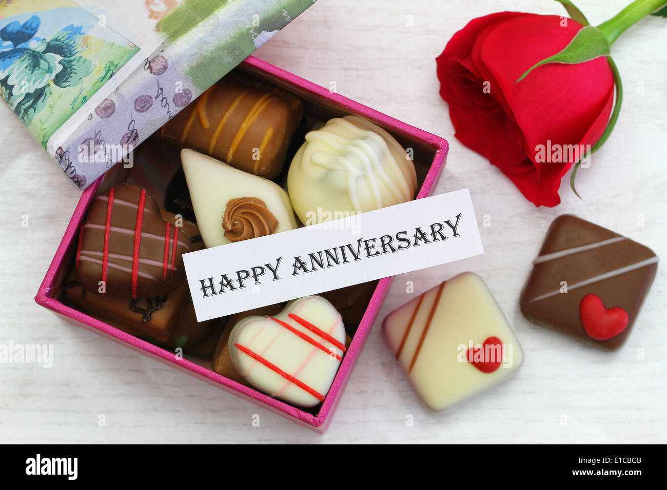 Feliz aniversario con chocolates y tarjeta rosa roja Foto de stock