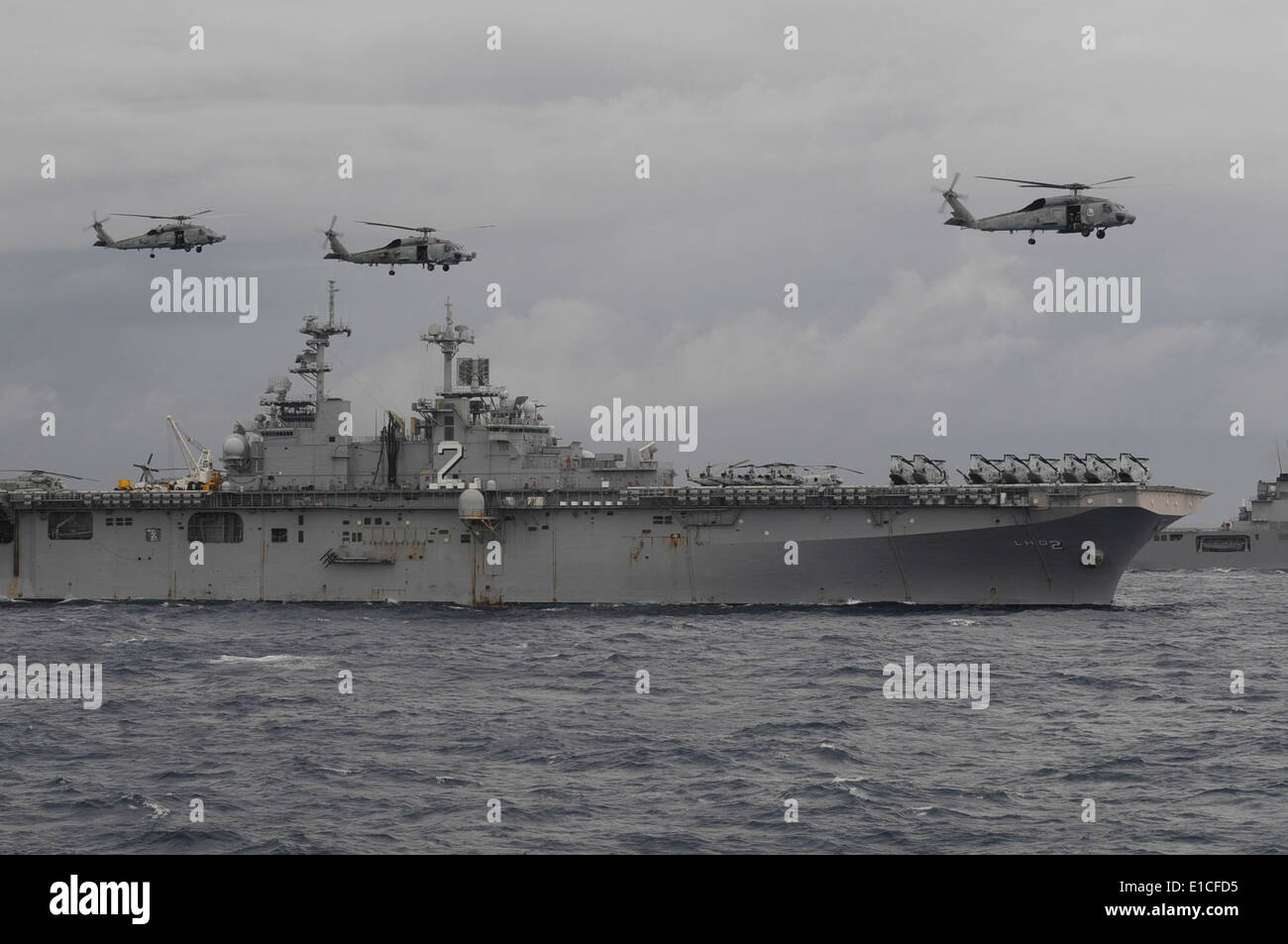 Helicópteros vuelan por encima del buque de asalto anfibio USS Essex (LHD 2) como maniobra hacia la formación durante el ejercicio anual (ANNUALEX Foto de stock