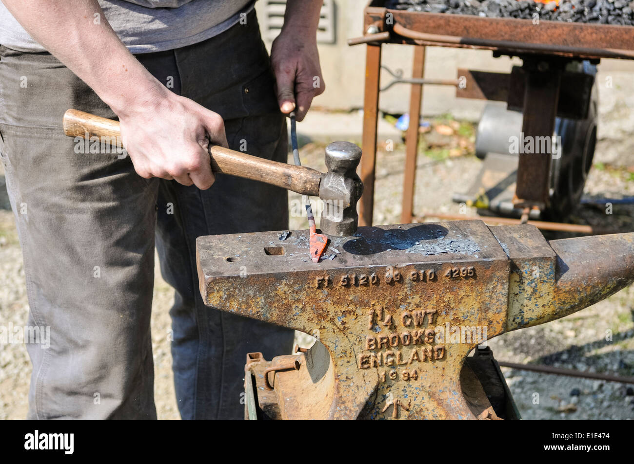 Herrero utiliza un martillo y un yunque para darle forma a una barra de  hierro Fotografía de stock - Alamy