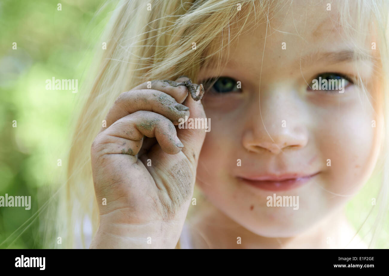 Niño rubia chica sujetando gusano fuera en el jardín, retrato, verano Foto de stock