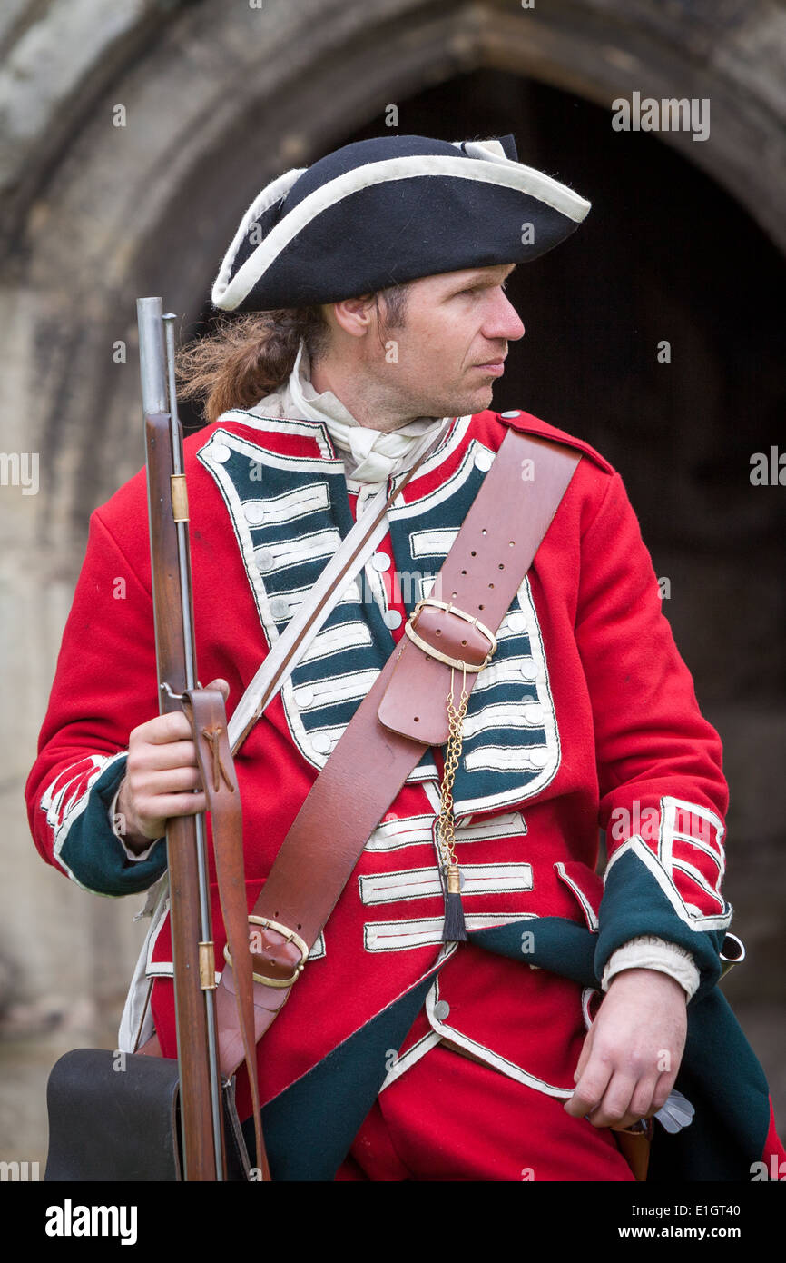 Un soldado vestido en Inglaterra en el siglo XVII tradicional casaca roja  uniforme del ejército llevando una flintlock musket fuera un castillo  entrada Fotografía de stock - Alamy