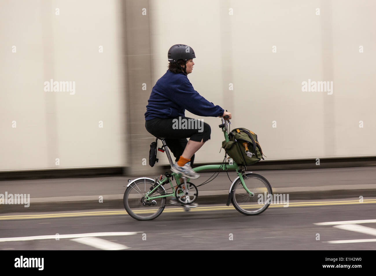 Mujer vistiendo un casco paseos su Brompton plegado bicicleta