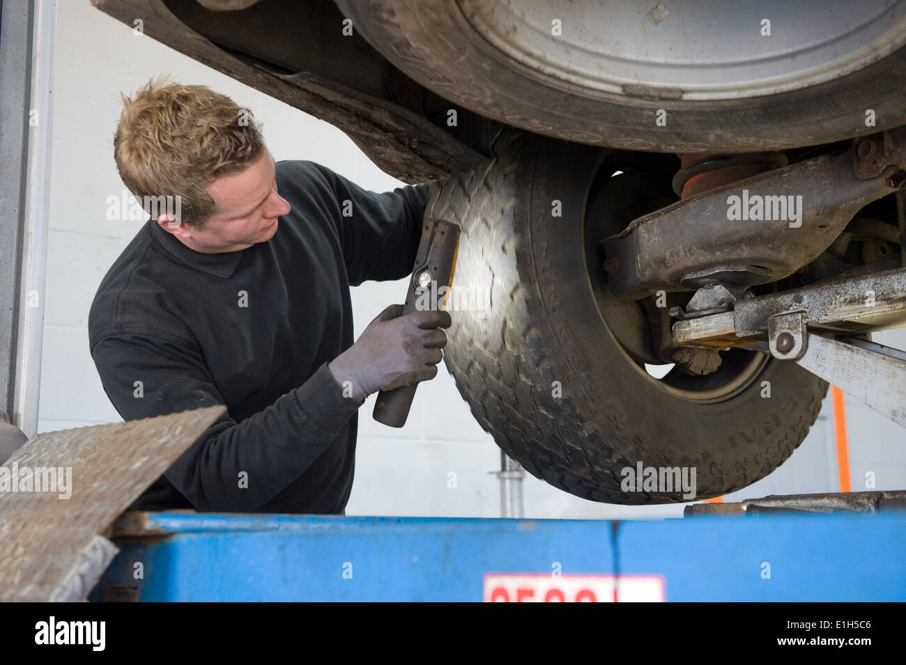Un mecánico está comprobando el perfil de un neumático de un coche levantado sobre un puente en un garaje. Foto de stock