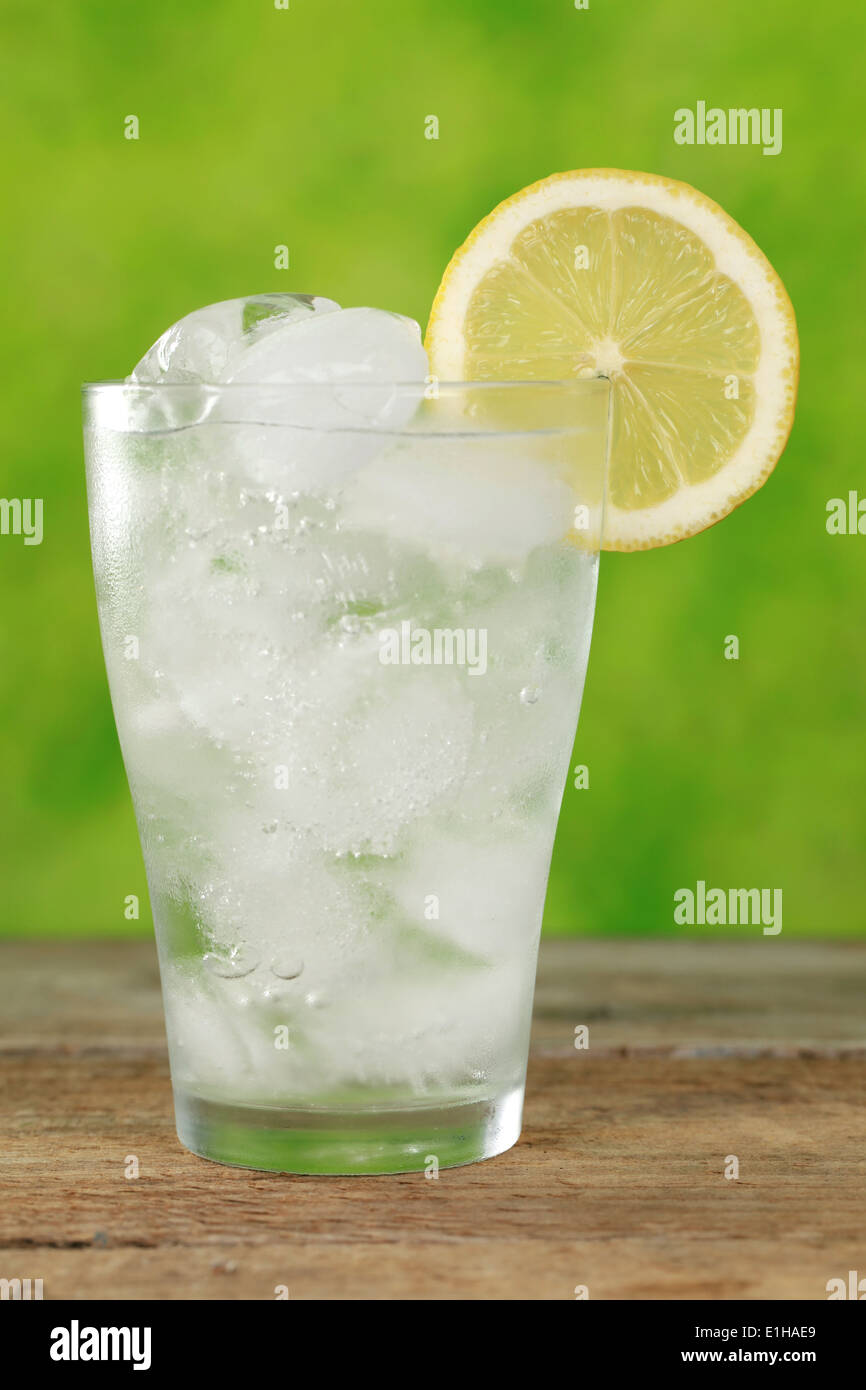 En un vaso de agua fría con cubitos de hielo, servido con un limón Foto de stock