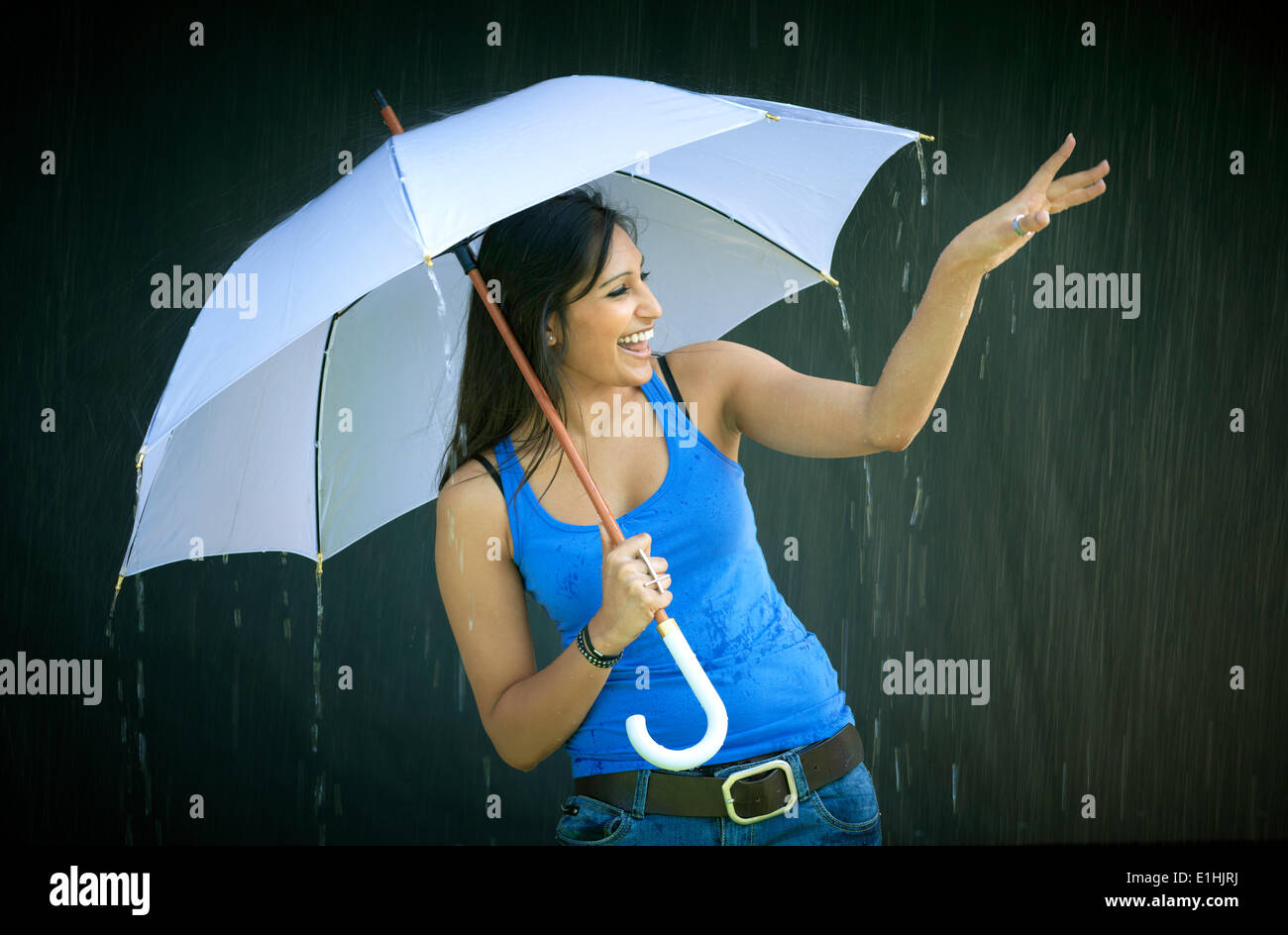 Mujer sonriente sosteniendo un paraguas, disfrutando de la lluvia Foto de stock