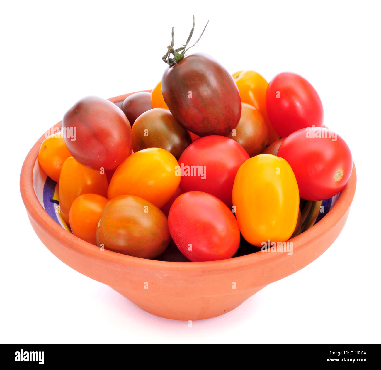 Un recipiente de barro con bebé tomates ciruela de diferentes colores sobre un fondo blanco. Foto de stock