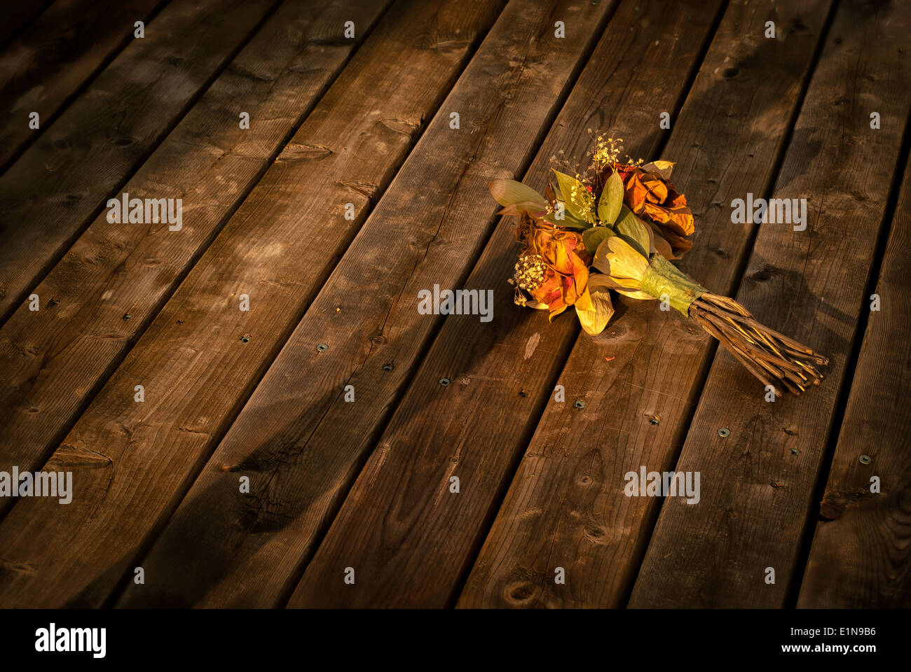 Un viejo y decoloración ramo de secado descartado flowerd reside en un piso de madera. Foto de stock