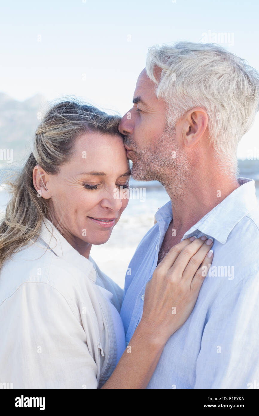 Hombre sonriente besando a su pareja en el frente en la playa. Foto de stock