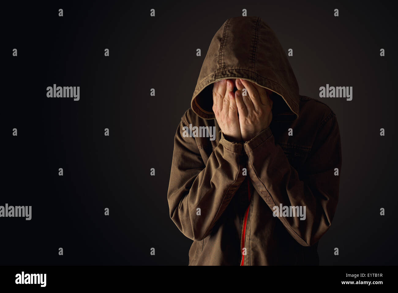 El hombre depresivo en chaqueta con capucha llorando con las manos cubriendo su rostro, mirando molesto y mostrar remordimiento Foto de stock