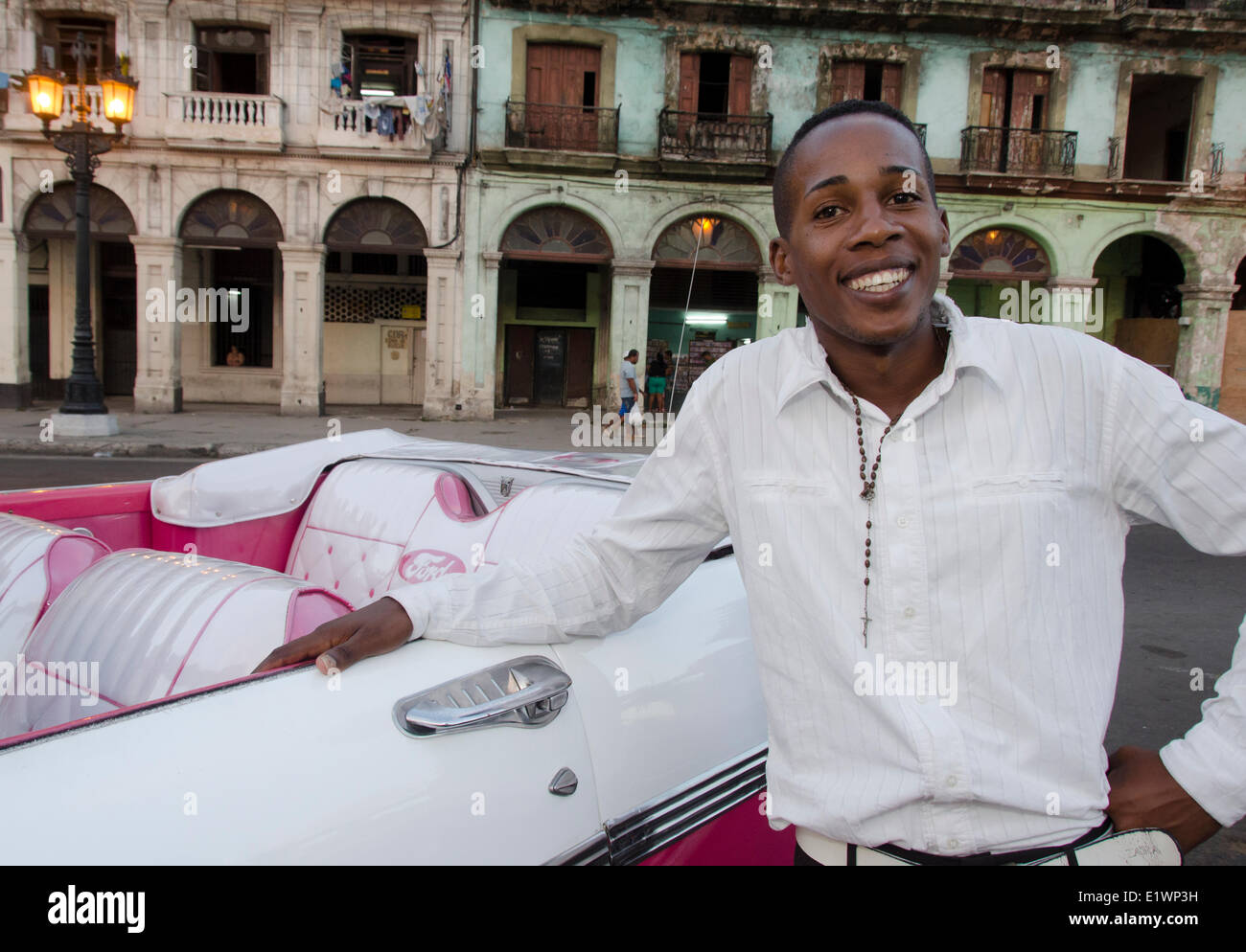Joven cubano conductor y coche clásico americano y las fachadas de los edificios antiguos, La Habana, Cuba CubaHavana Foto de stock