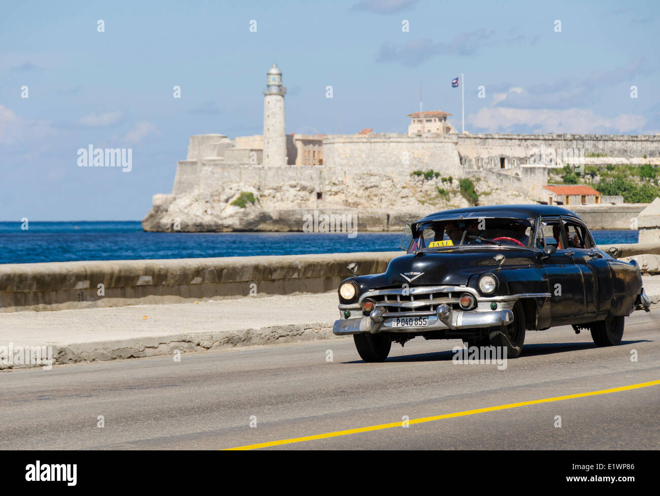 Coches clásicos americanos alomg detrás es el malecón, Castillo del Morro, una pintoresca fortaleza vigilando la entrada a la bahía de La Habana, hav Foto de stock