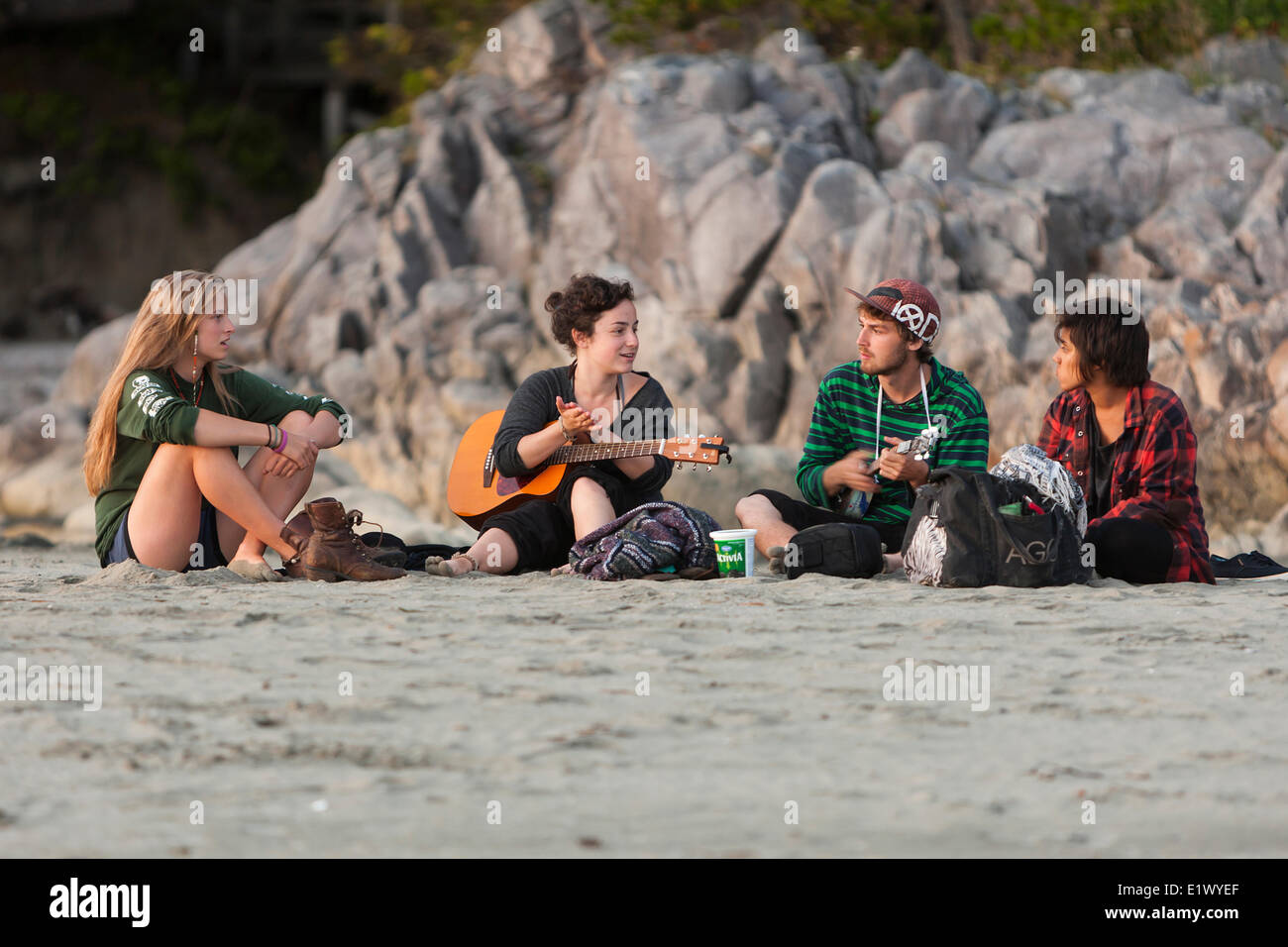 Cuatro amigos se reúnen para reproducir música y socializar en Tonquin Park en Tofino. Tofino, Vancouver Island, British Columbia, Canadá Foto de stock