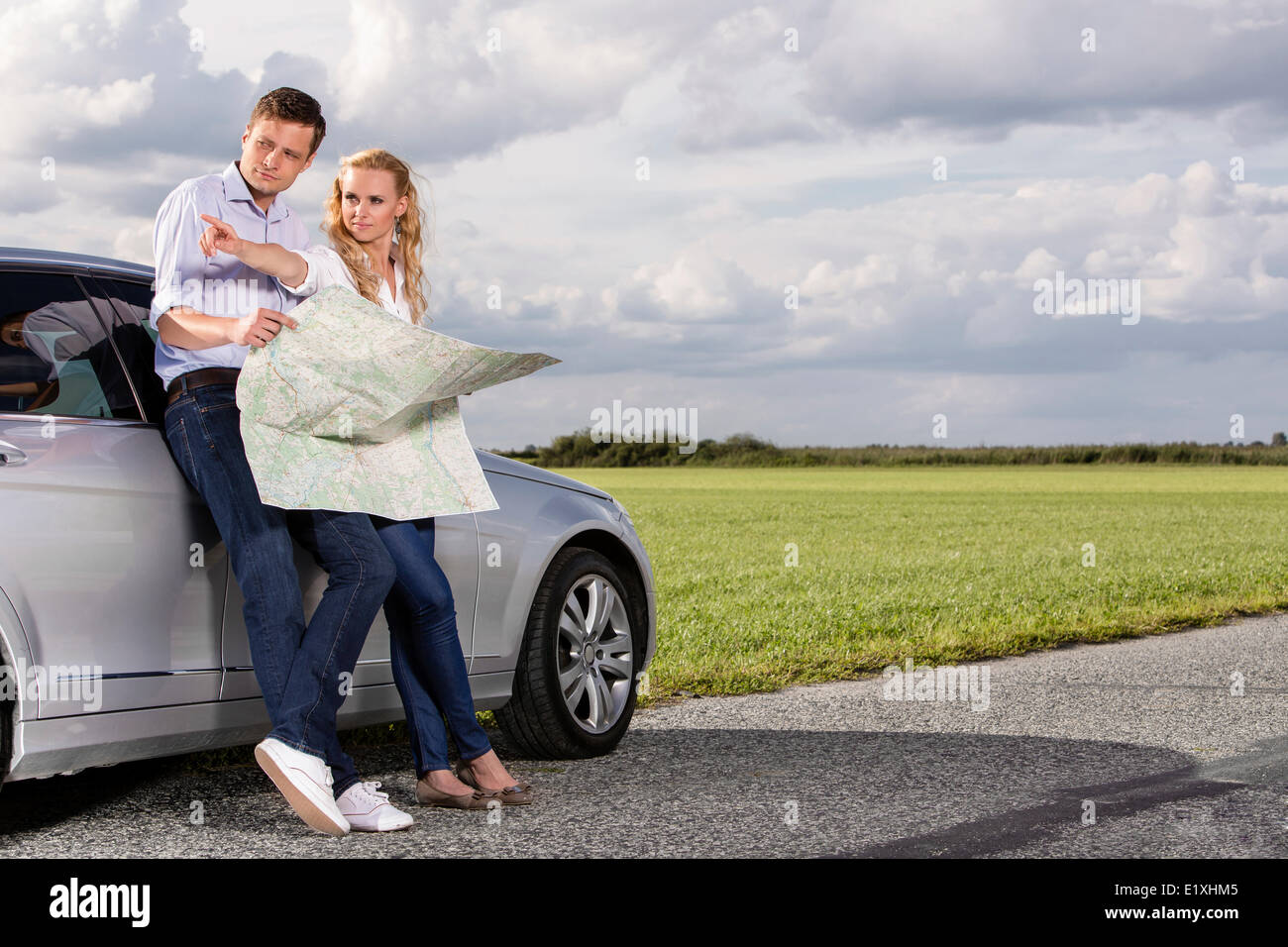 La longitud completa de la pareja discutiendo con mapa de dirección mientras recostado en coche en campo Foto de stock