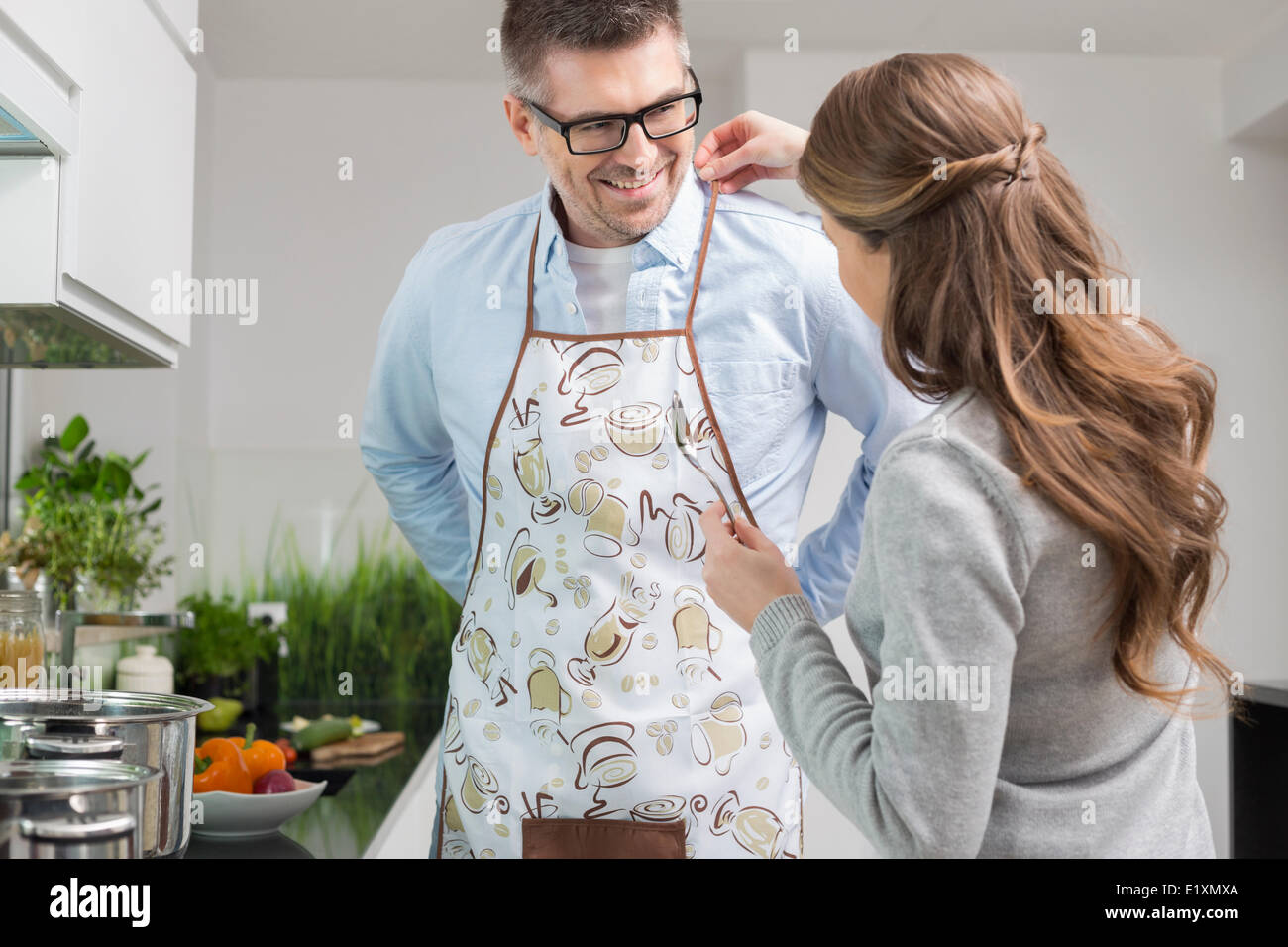 Mujer ayudando al hombre a poner el delantal en la cocina Foto de stock