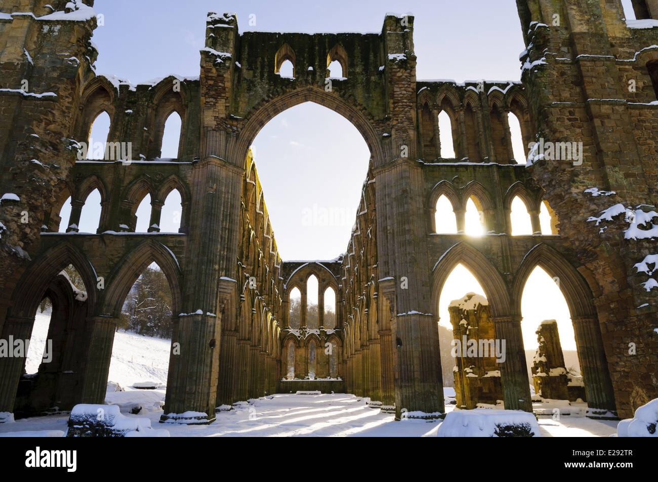 La luz del sol brillando a través de ventanas arqueadas del arruinado abadía cisterciense en nieve, Rievaulx Abbey, North York Moros N.P., North Yorkshire, Inglaterra, enero Foto de stock