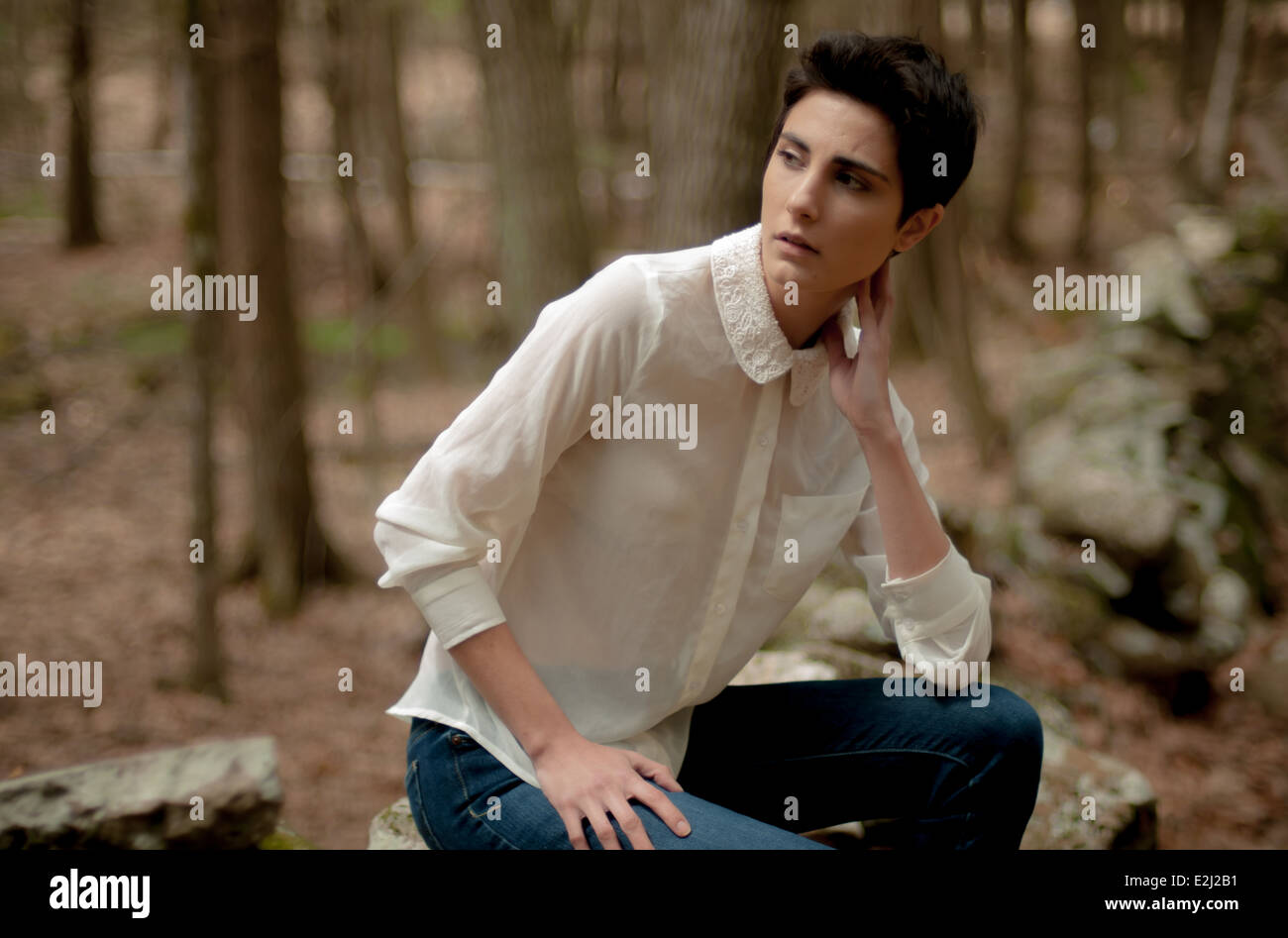 Una mujer joven con el pelo corto, oscuro, llevaba una blusa blanca y  pantalones de mezclilla, sentada sola en un antiguo muro de piedra en el  bosque Fotografía de stock - Alamy