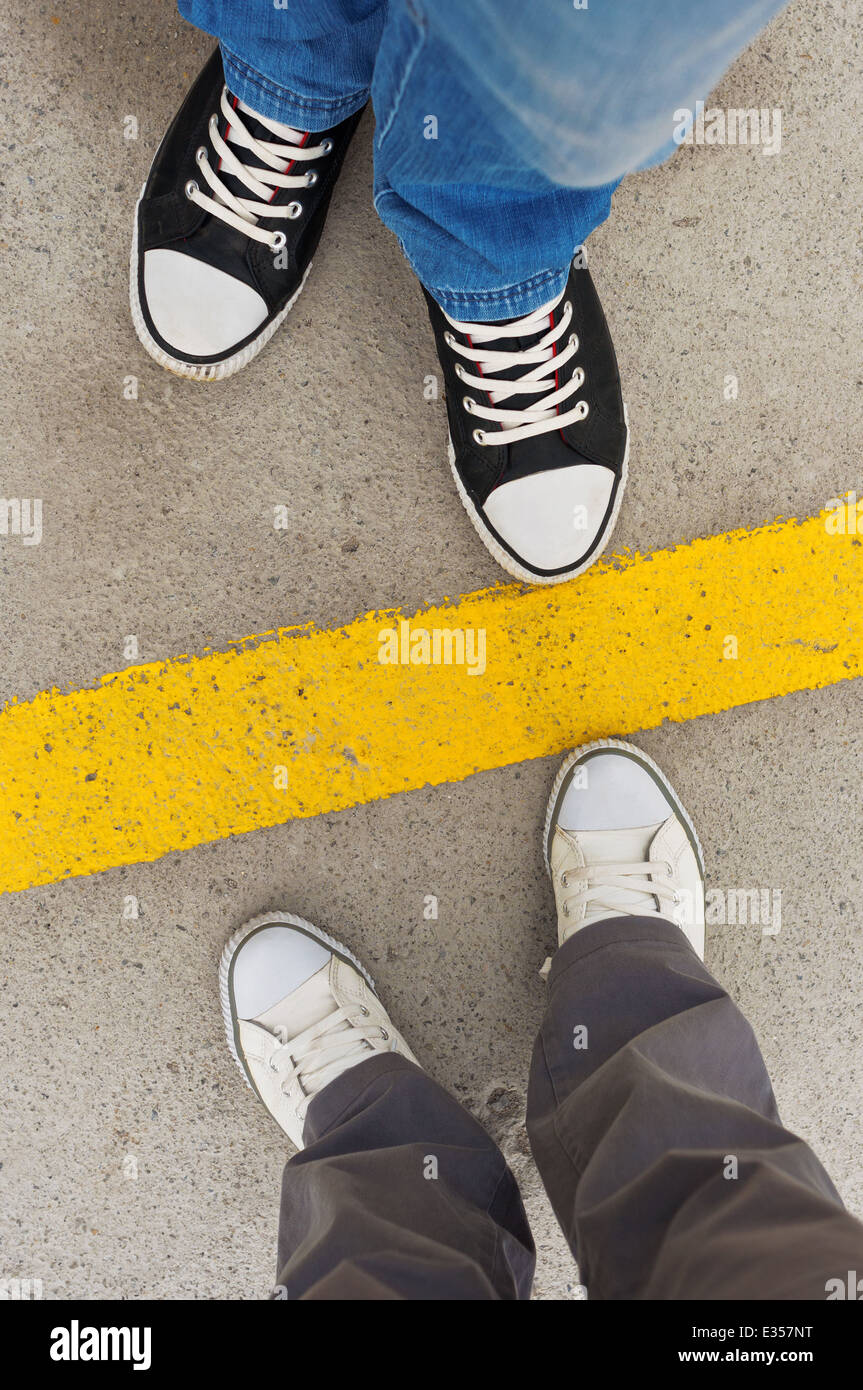 Sneakers desde arriba. Pies masculinos y femeninos en zapatillas desde arriba, de pie en la línea divisoria. Foto de stock