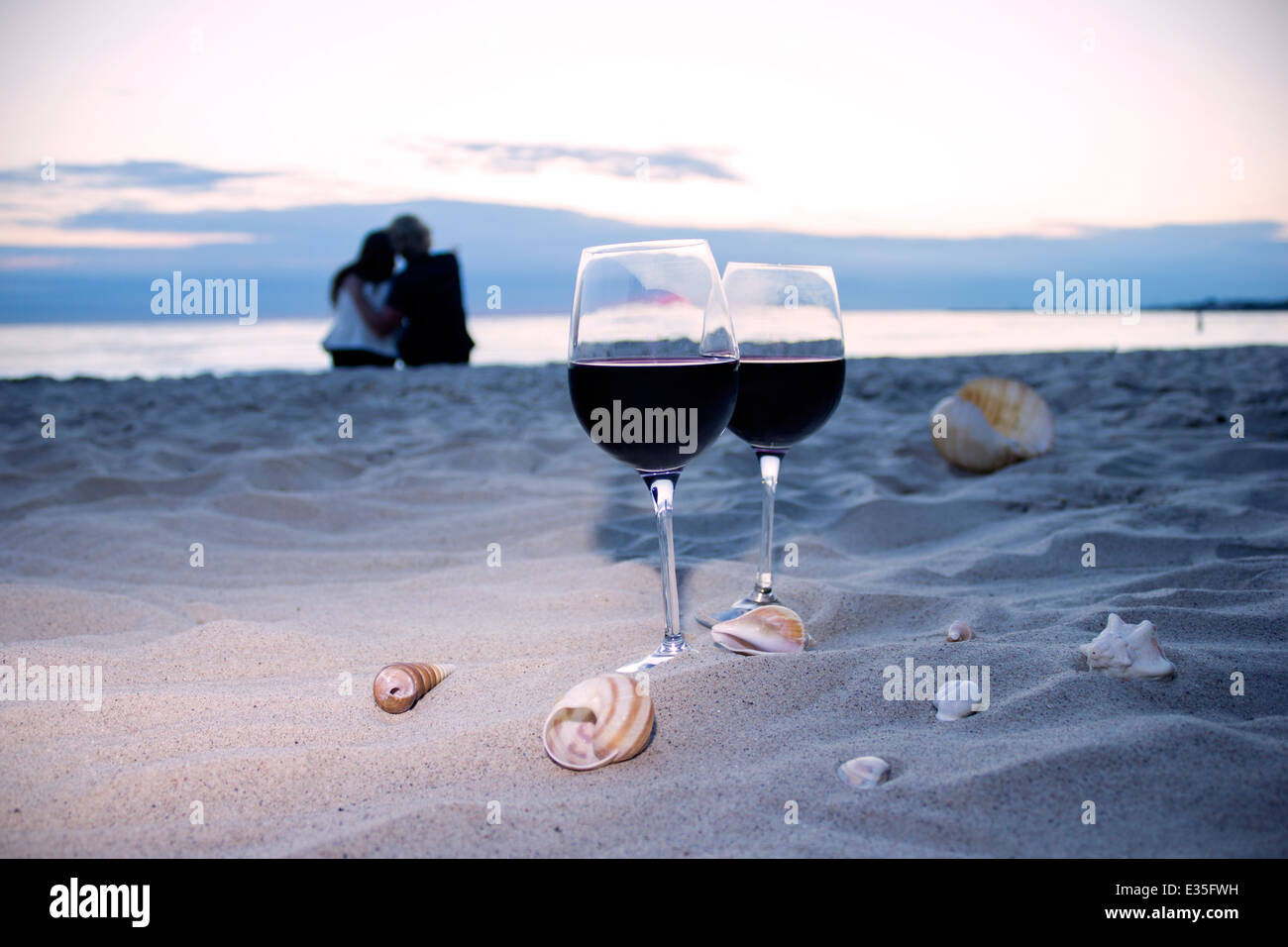 Noche romántica en la playa en el atardecer: dos copas de vino, velas, conchas, Día de San Valentín Foto de stock