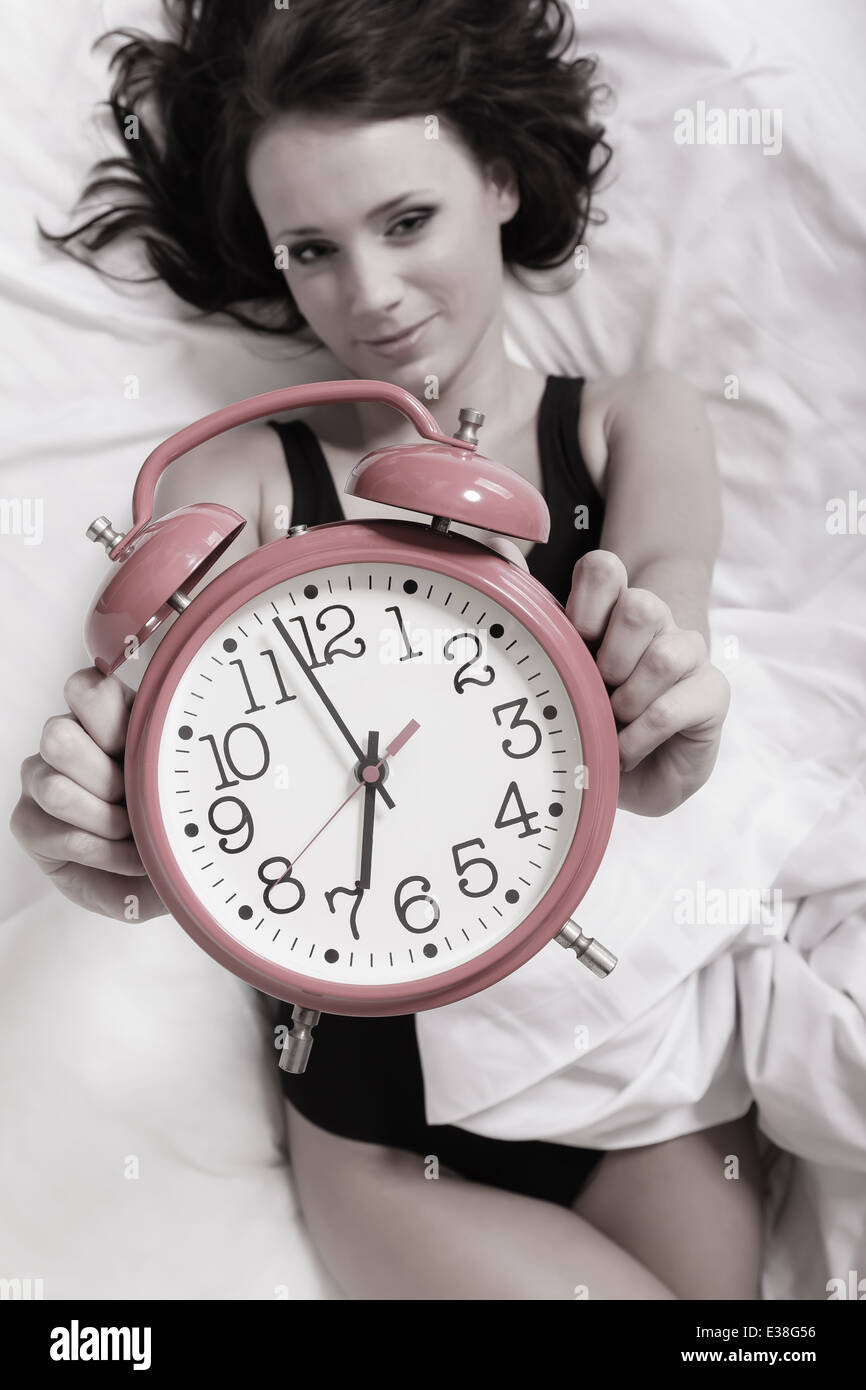 Reloj de alarma en manos femeninas. Mujer sexy girl perezoso tumbado en la  cama y mostrando la hora Fotografía de stock - Alamy