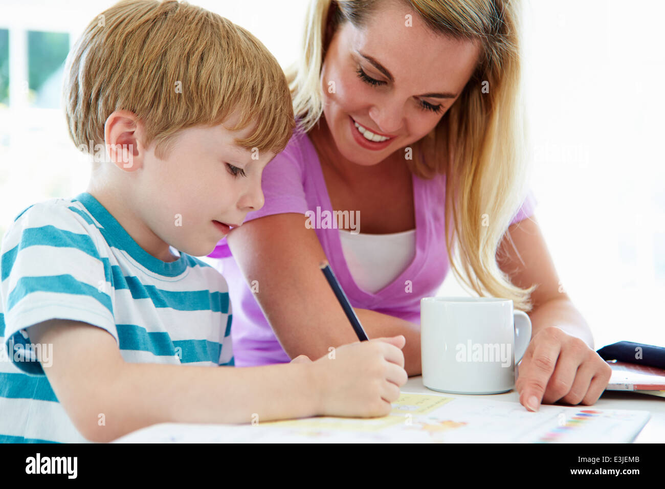 Hijo de madre ayudando con las tareas escolares en la cocina Foto de stock